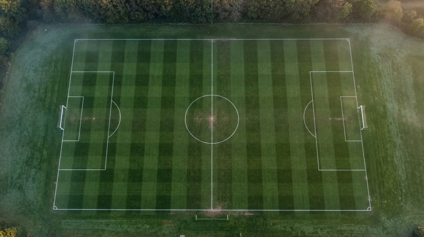 Ein Fussballplatz von oben gesehen, die Linien bilden ein helles Muster auf dem Rasen, Drohnenperspektive in der Morgendämmerung.