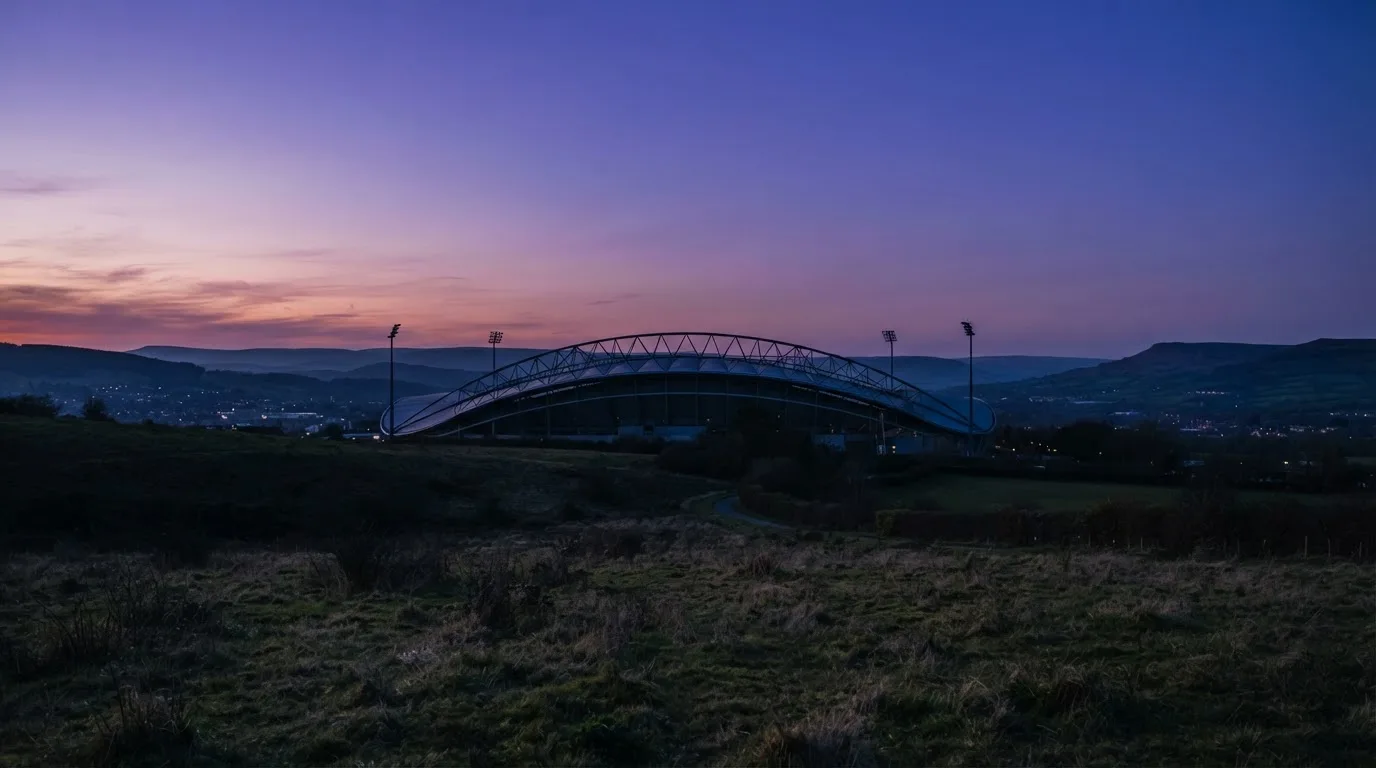 Die Silhouette eines Stadiondachs vor dem violetten Abendhimmel, dahinter eine Hügelkette.