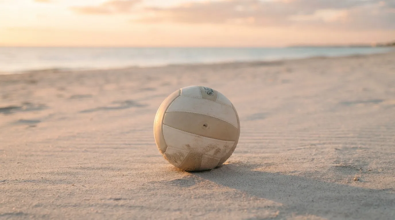 Ein Volleyball liegt auf feinem Sand an einem leeren Strand bei Sonnenaufgang.