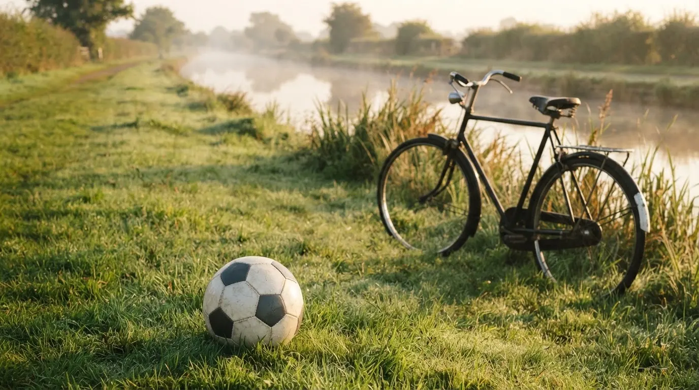 Ein Fussball liegt auf einer Wiese neben einem Fahrrad, im Hintergrund ein Kanal im Morgenlicht