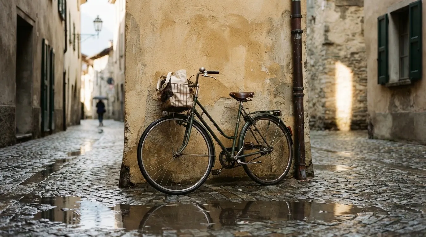 Ein Fahrrad lehnt an einer Mauer in einer Altstadtgasse, das Kopfsteinpflaster glänzt nass nach dem Regen.