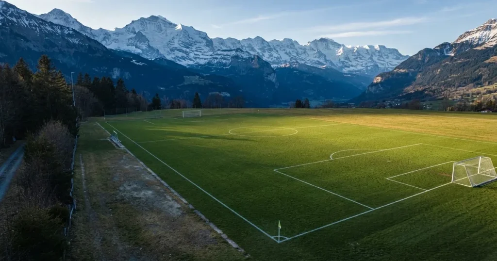Ein Fussballplatz aus der Vogelperspektive mit sauberen Linien auf dichtem Rasen, in der Ferne verschneite Berge.