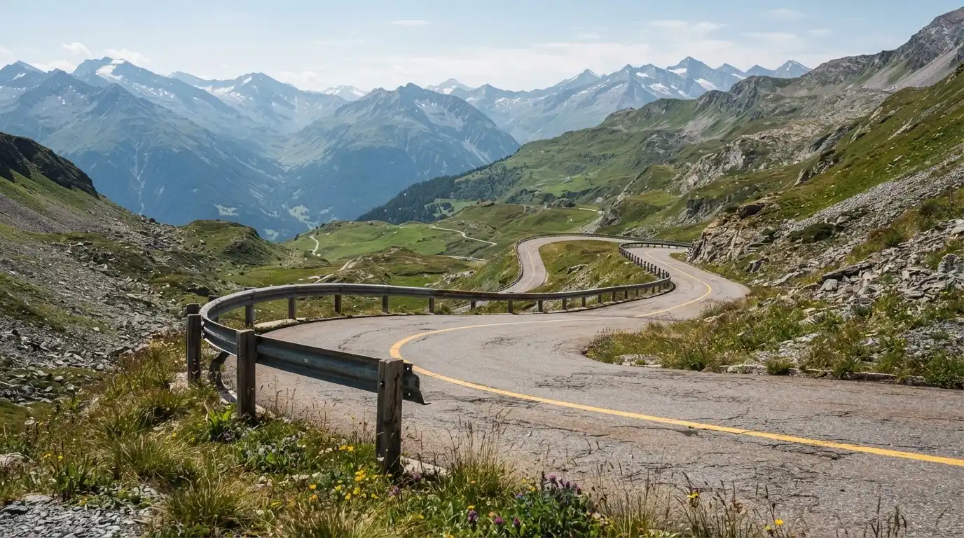 Eine Passstrasse mit Leitplanke windet sich an einem klaren Tag durch eine Berglandschaft.