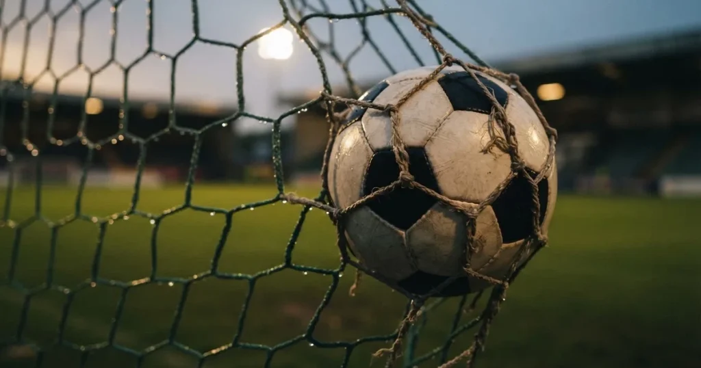 Ein Fussballnetz in Nahaufnahme, in dem ein Ball hängt, Wassertropfen glänzen auf den Maschen.