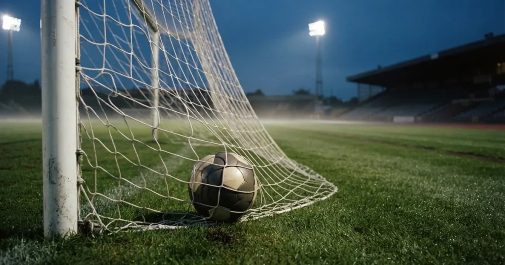 Ein Fussball liegt im Netz eines Tores, Flutlicht und kalte Abendluft liegen über dem leeren Platz