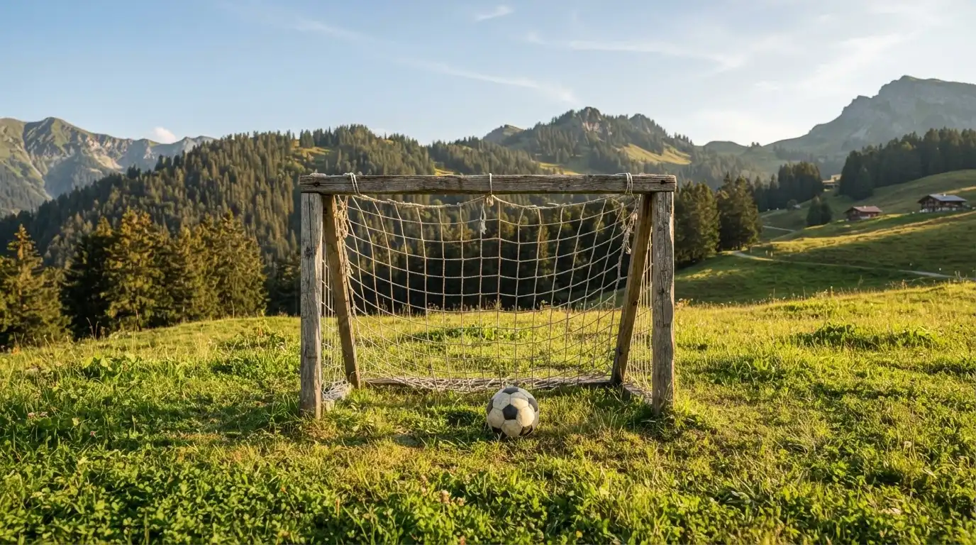 Eine Almwiese mit einem kleinen Holztor für Kinderfussball, dahinter erheben sich bewaldete Hänge im Nachmittagslicht.