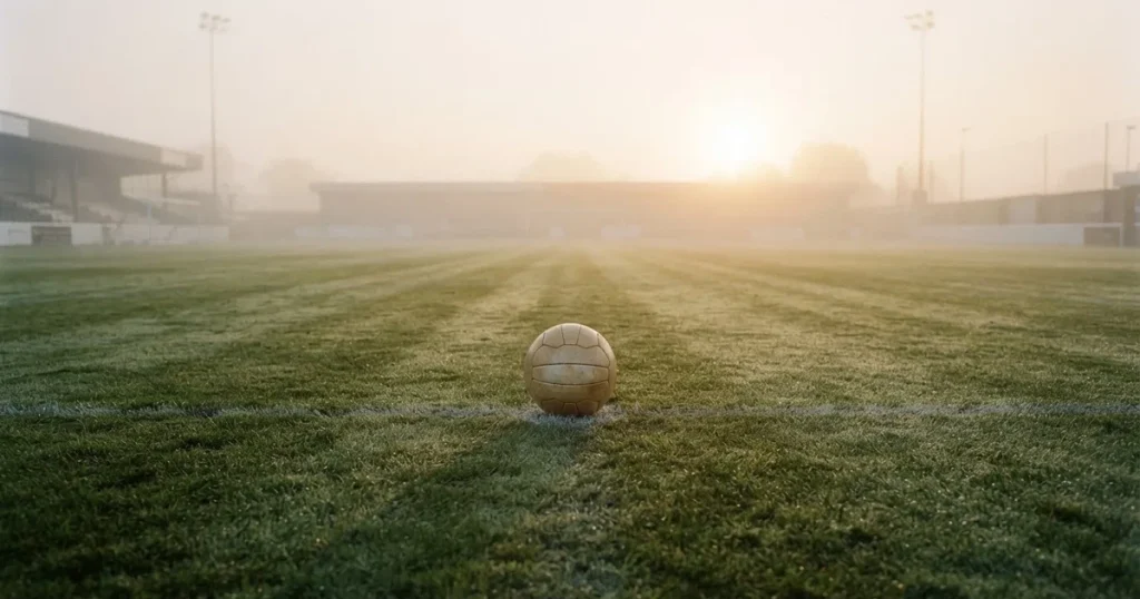 Ein Fussball liegt auf dem Anstosspunkt eines leeren Rasenplatzes im dichten Morgennebel.